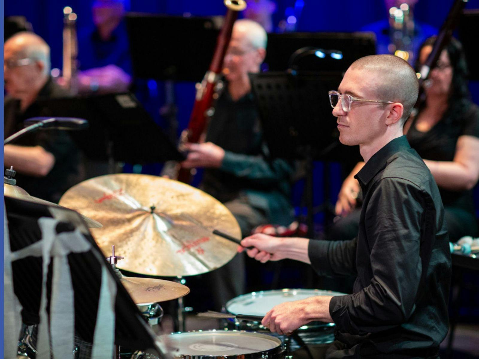 member of the orchestra man in front playing drums and background players