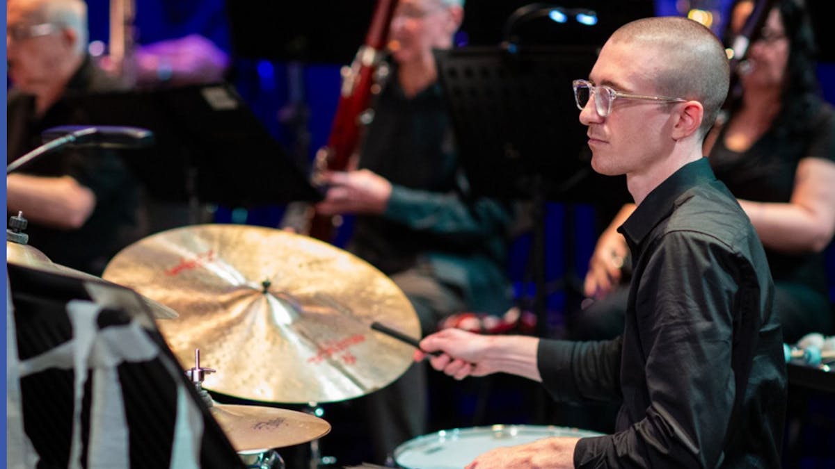 member of the orchestra man in front playing drums and background players