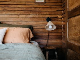 The bed dressed in mismatched linen and set against a warm timber cladded wall