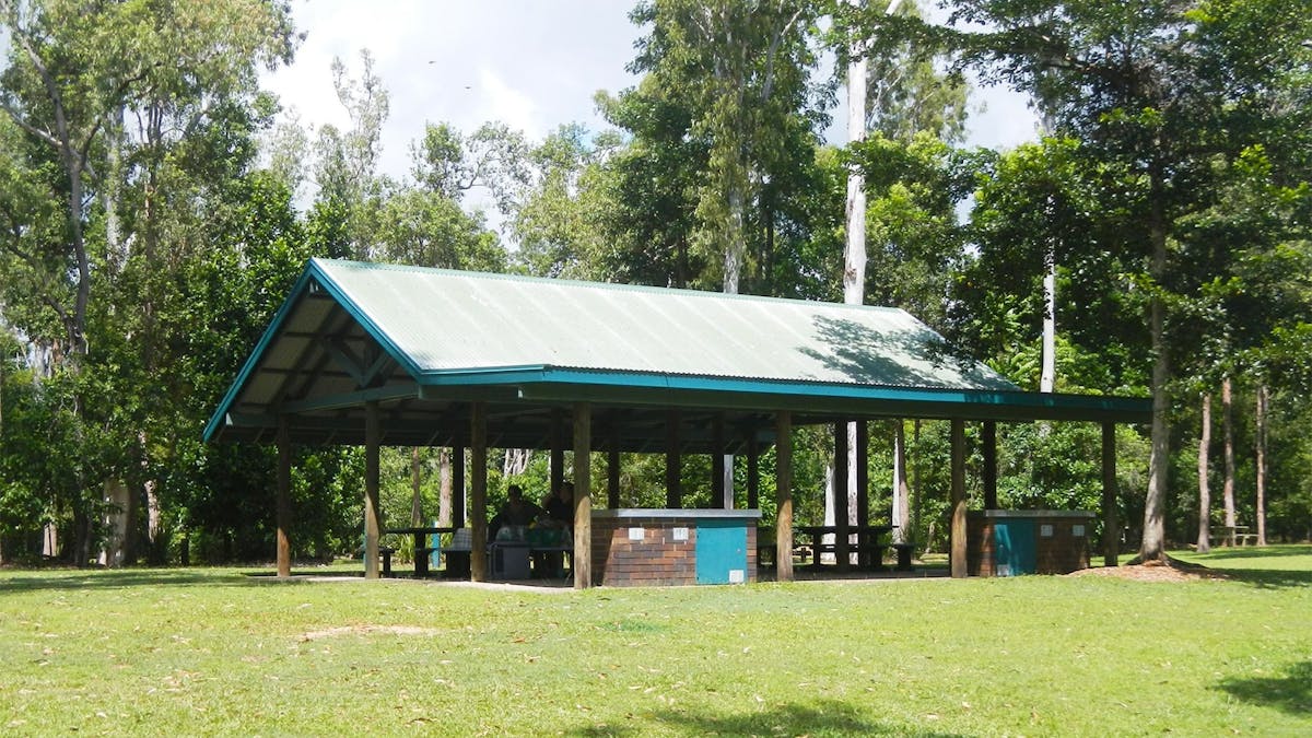 Sheltered picnic area amongst grassy field surrounded by shady trees
