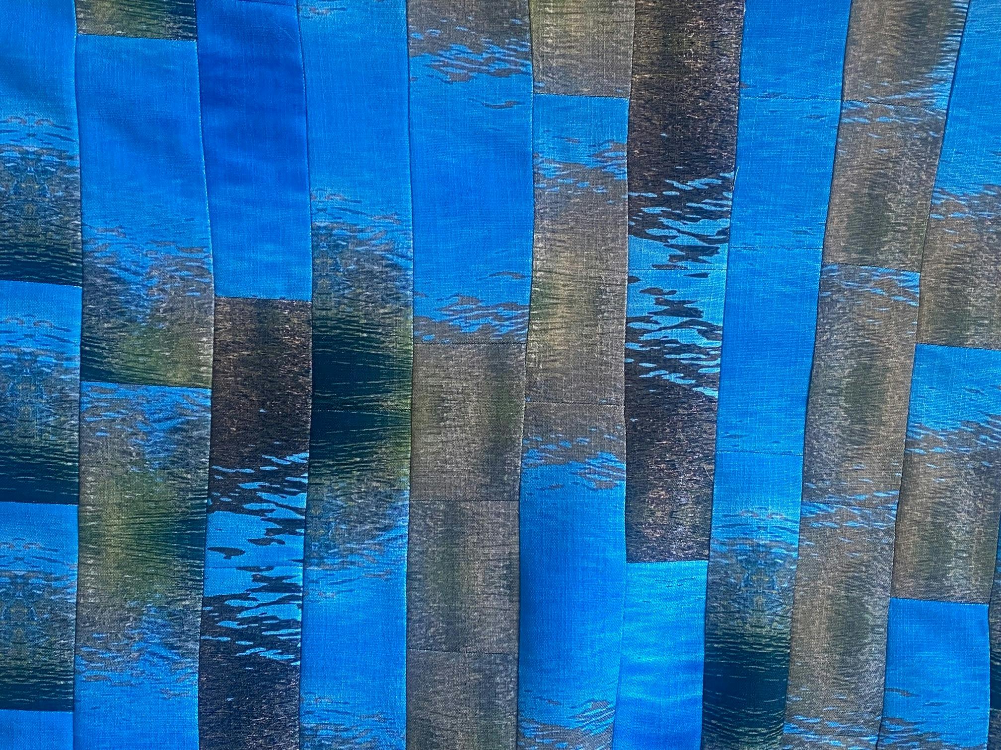 A quilt made up of thin strips of fabric, with an abstracted motif of ripples in water.