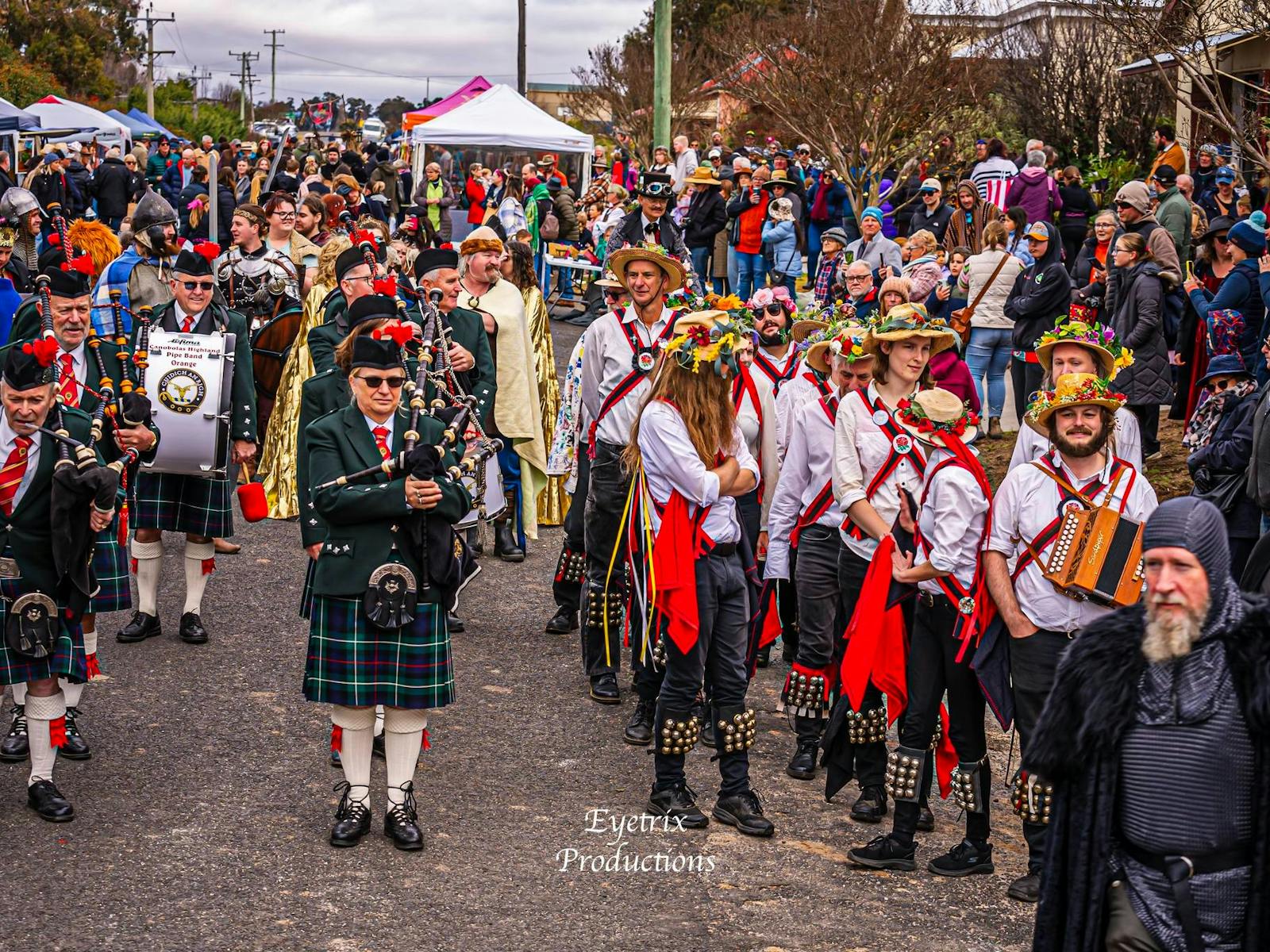 a crowd market scene with pipers, drummers and morris dancers in the foreground
