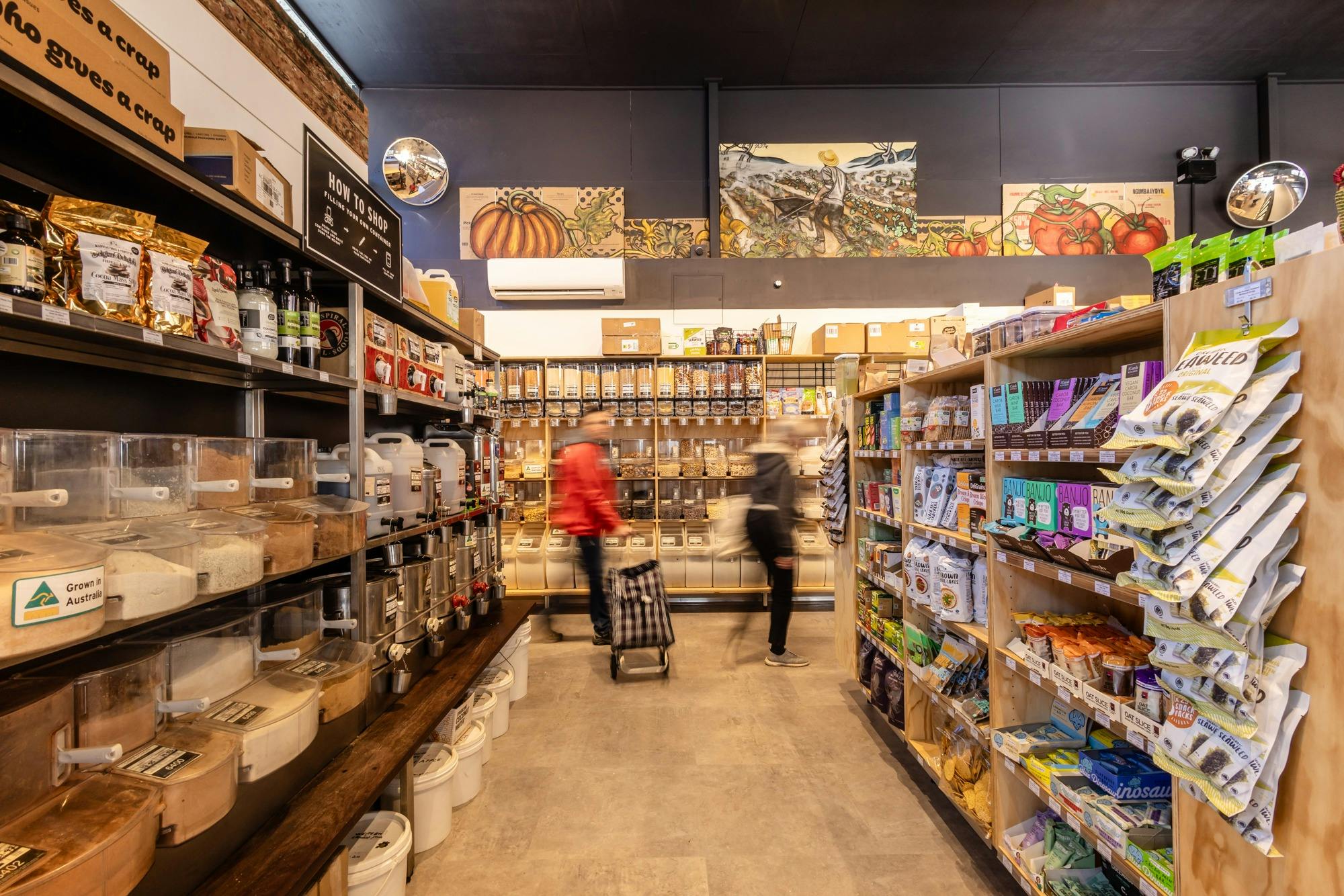 Bulk and packaged foods line the shelves, blurred people walk by