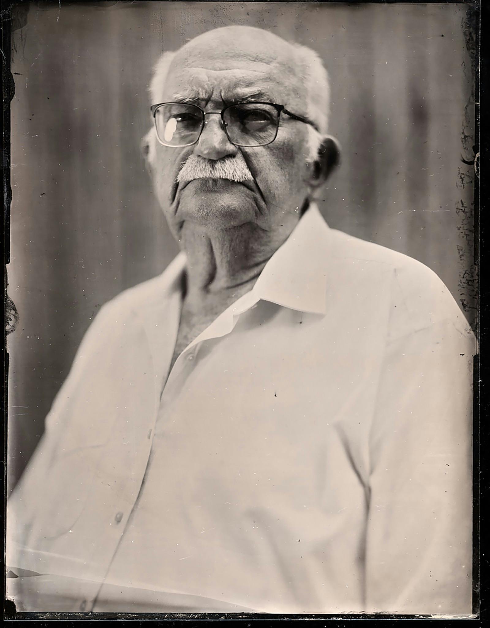A black and white photograph of a man with a white mustache and glasses