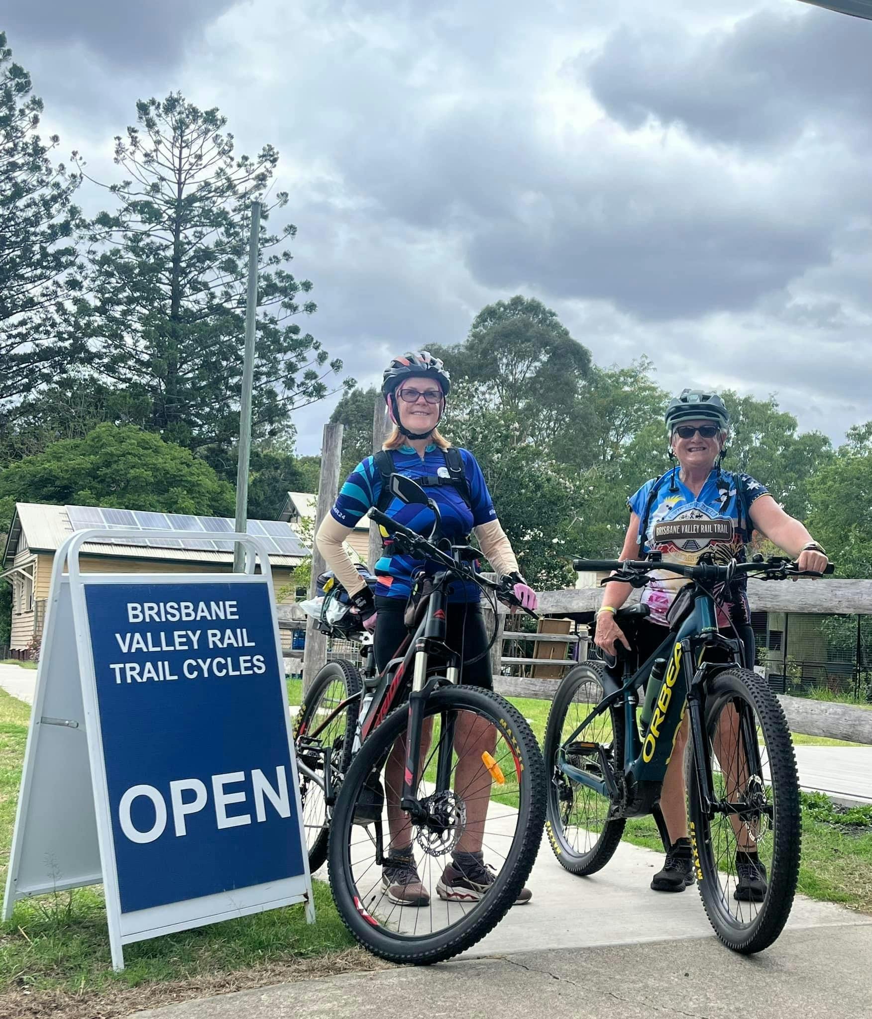 two bicycle riders standing beside their electric bikes and a sign