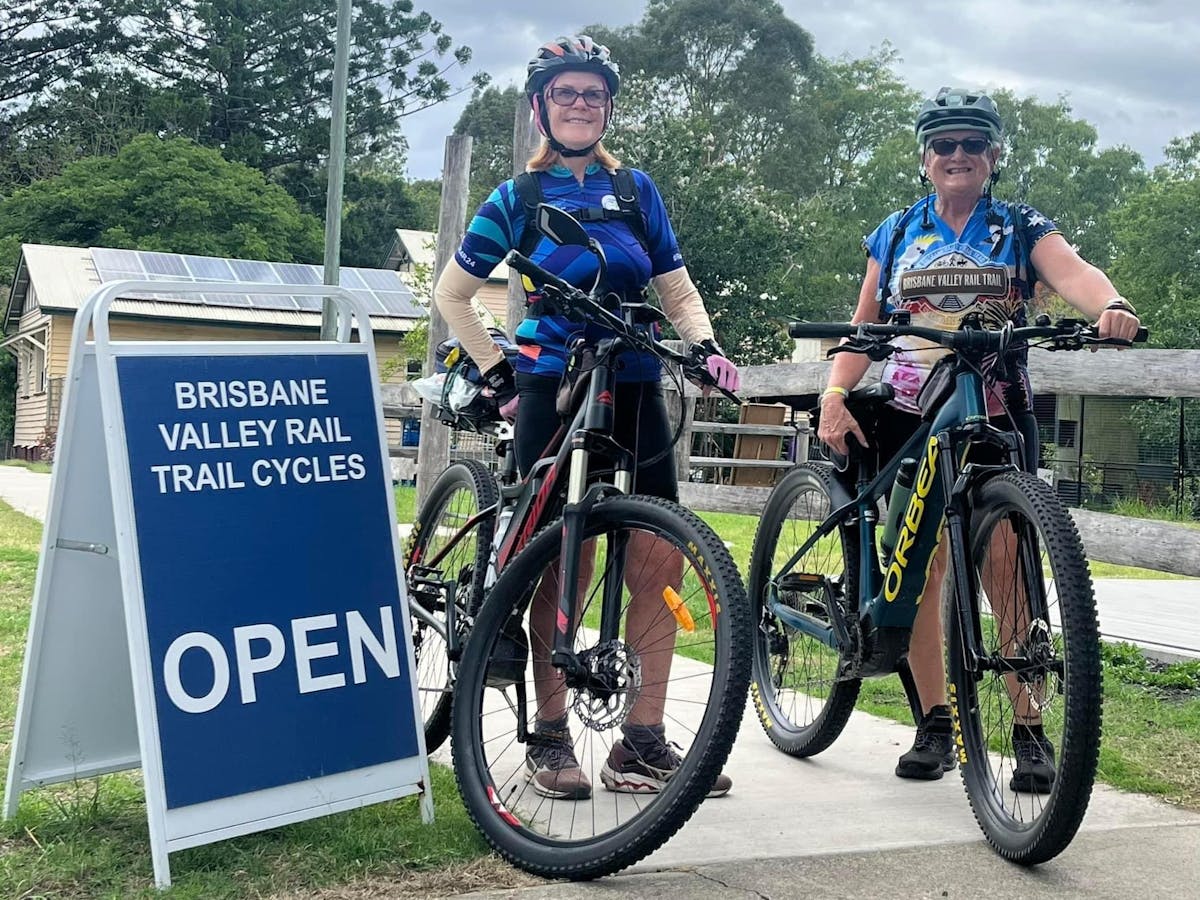 two bicycle riders standing beside their electric bikes and a sign