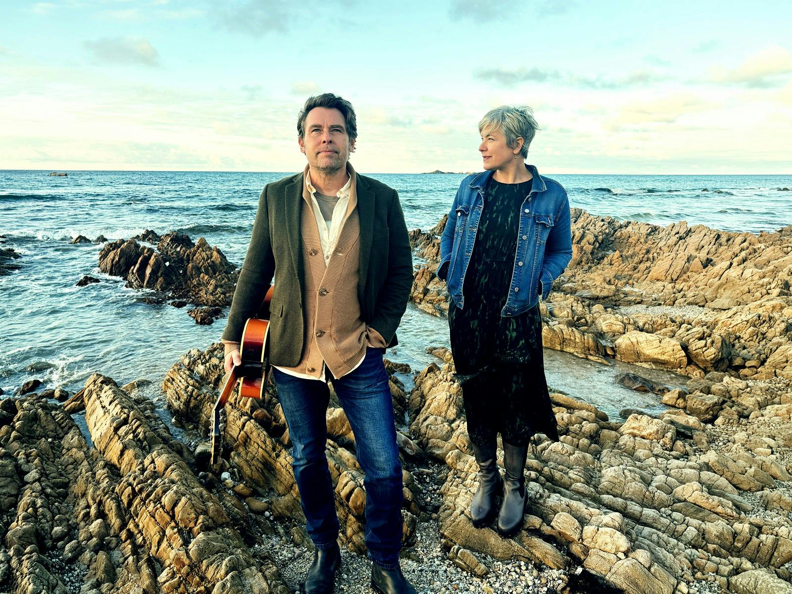 A man and a woman standing on rocks beside the ocean