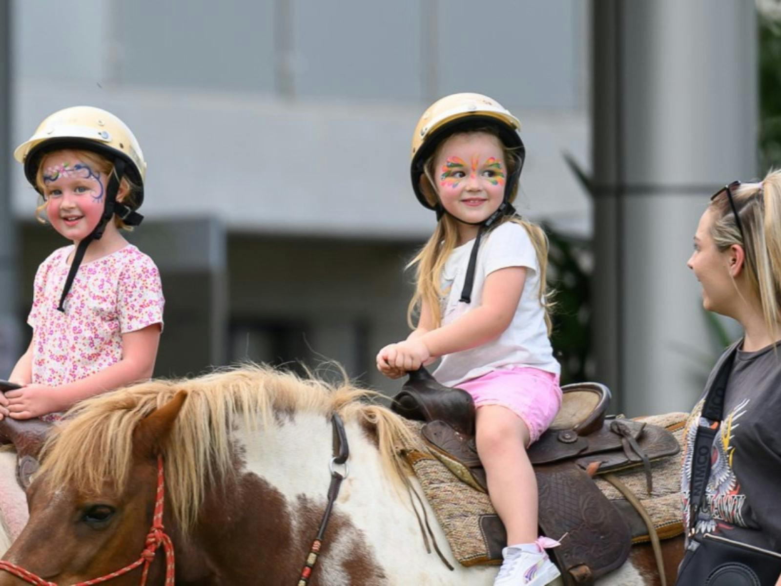 Two girls riding horses with an adult supervising on the side