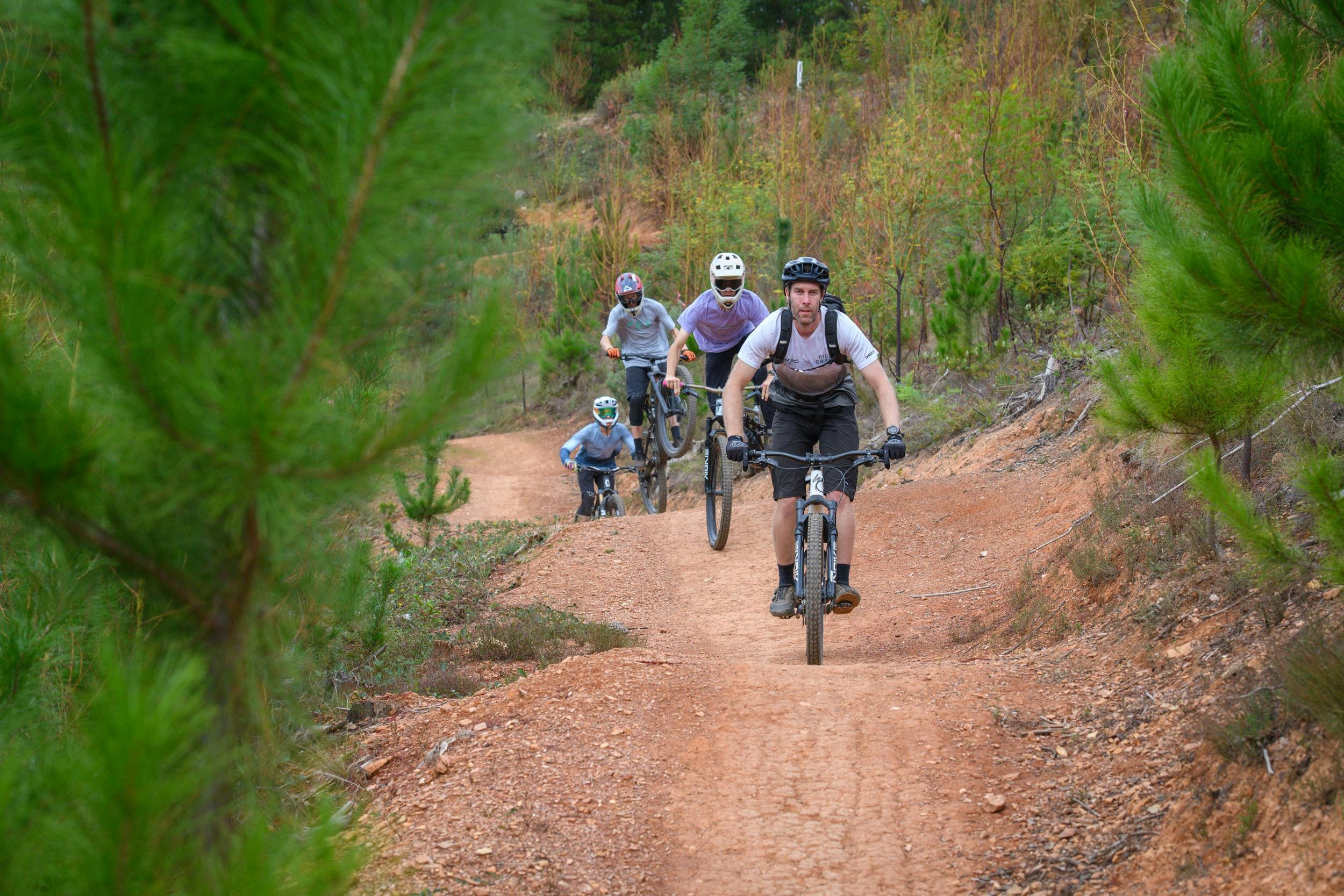 A group of mountain bikers roll down a mountain bike trail following a guide on a bike.