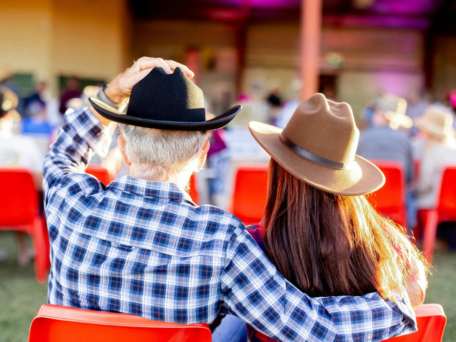 Male and female wearing cowboy hats. Image taken on their backs with event atmosphere in the back
