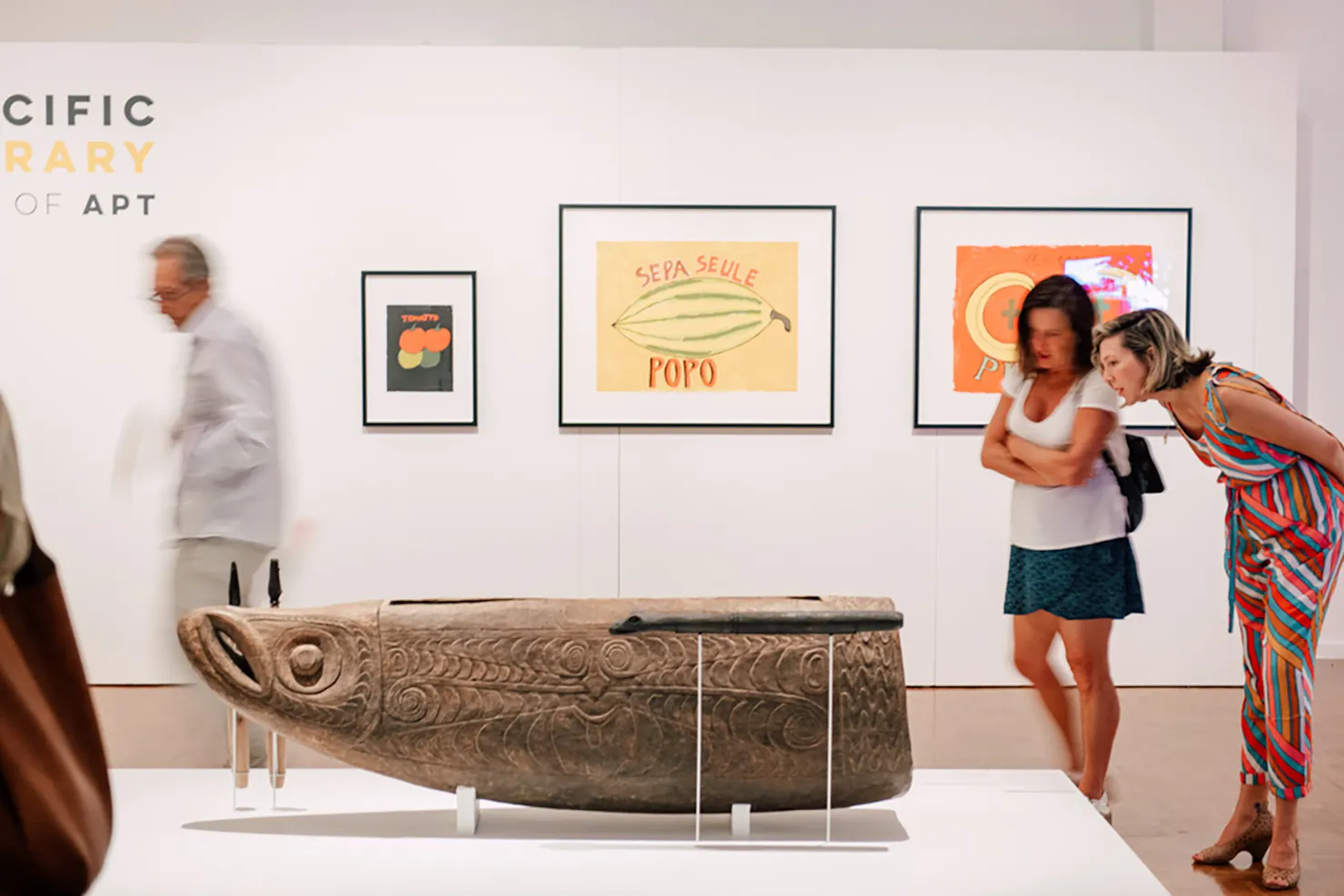 two women inspect a wooden carved sculpture of an indigenous fish god