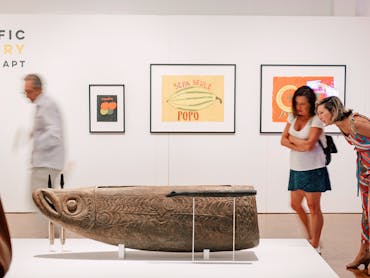 two women inspect a wooden carved sculpture of an indigenous fish god two women inspect a wooden carved sculpture of an indigenous fish god