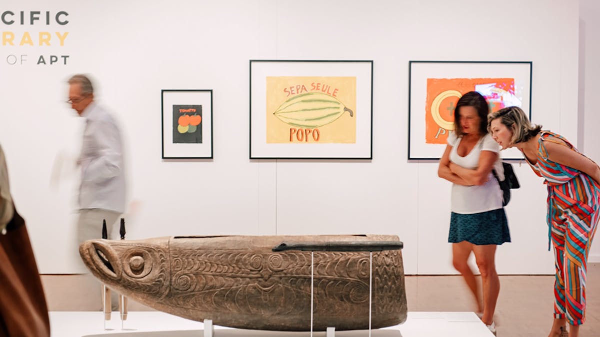 two women inspect a wooden carved sculpture of an indigenous fish god
