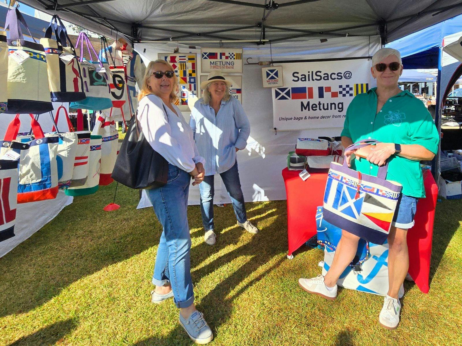Market stall of tote bags made from recycled yacht sails with three ladies standing in stall