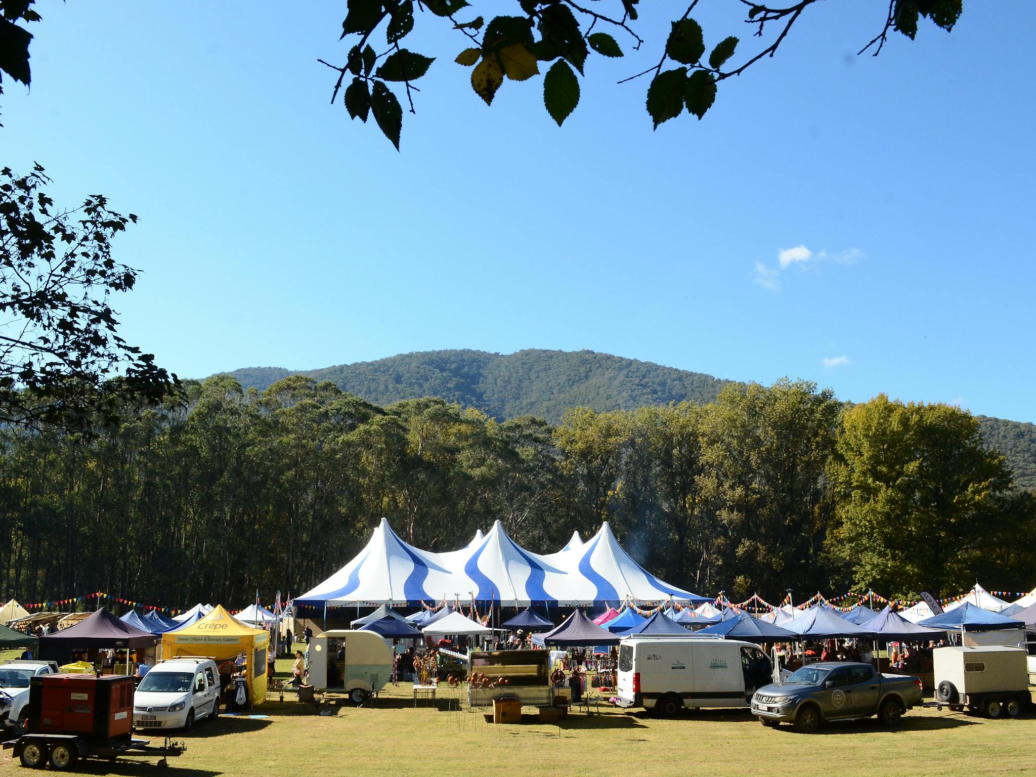 Landscape view of the the festival site with stalls and the big tent with a tree covered mountain