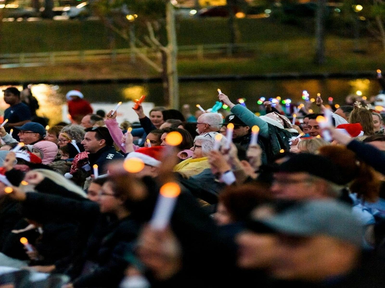 A tight crowd of people wave candles in the air. The river is behind them.