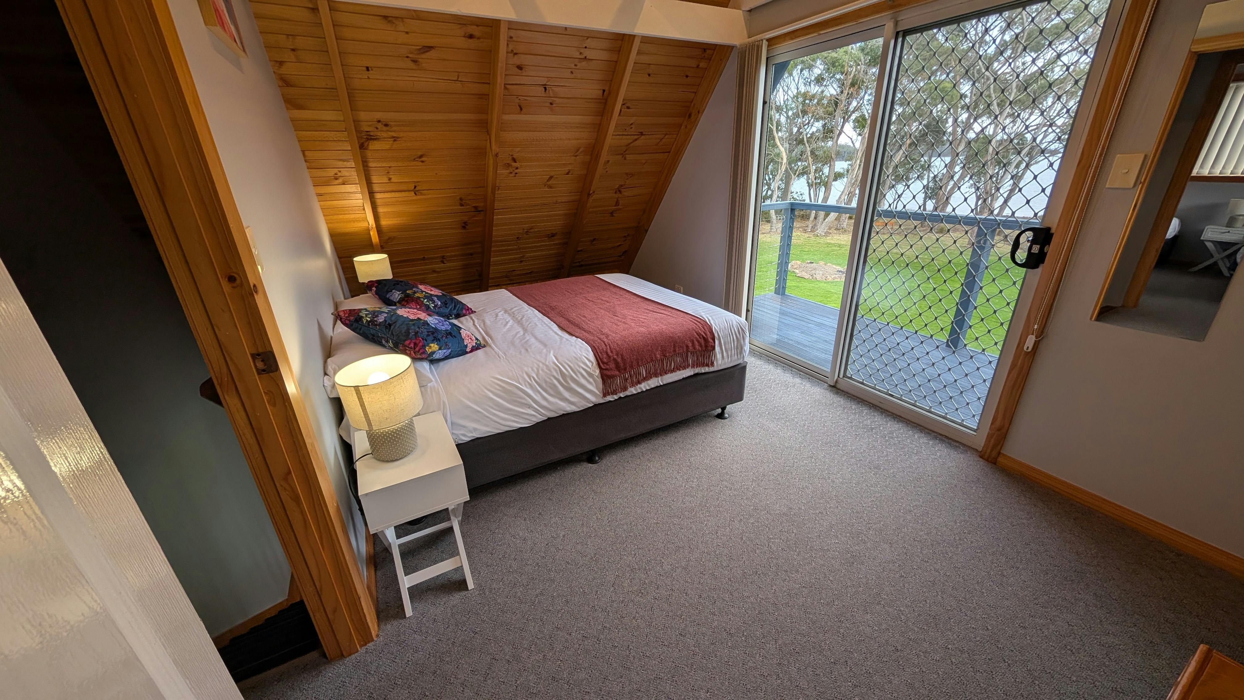 Bedroom with queen bed, balcony access, garden outlook and water views.