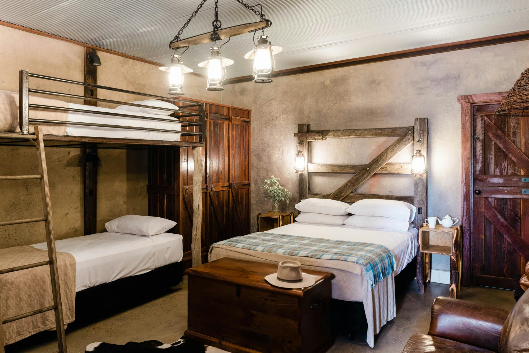 Bunk beds and king sized bed inside rustic looking room with timber headboards and cupboard