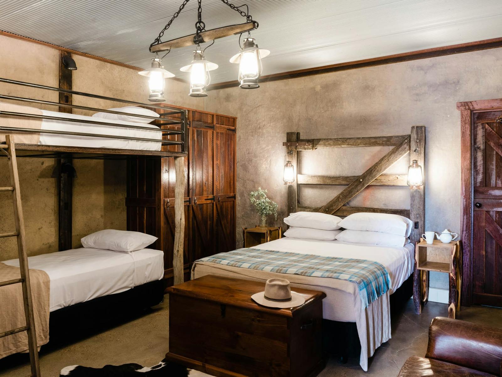 Bunk beds and king sized bed inside rustic looking room with timber headboards and cupboard