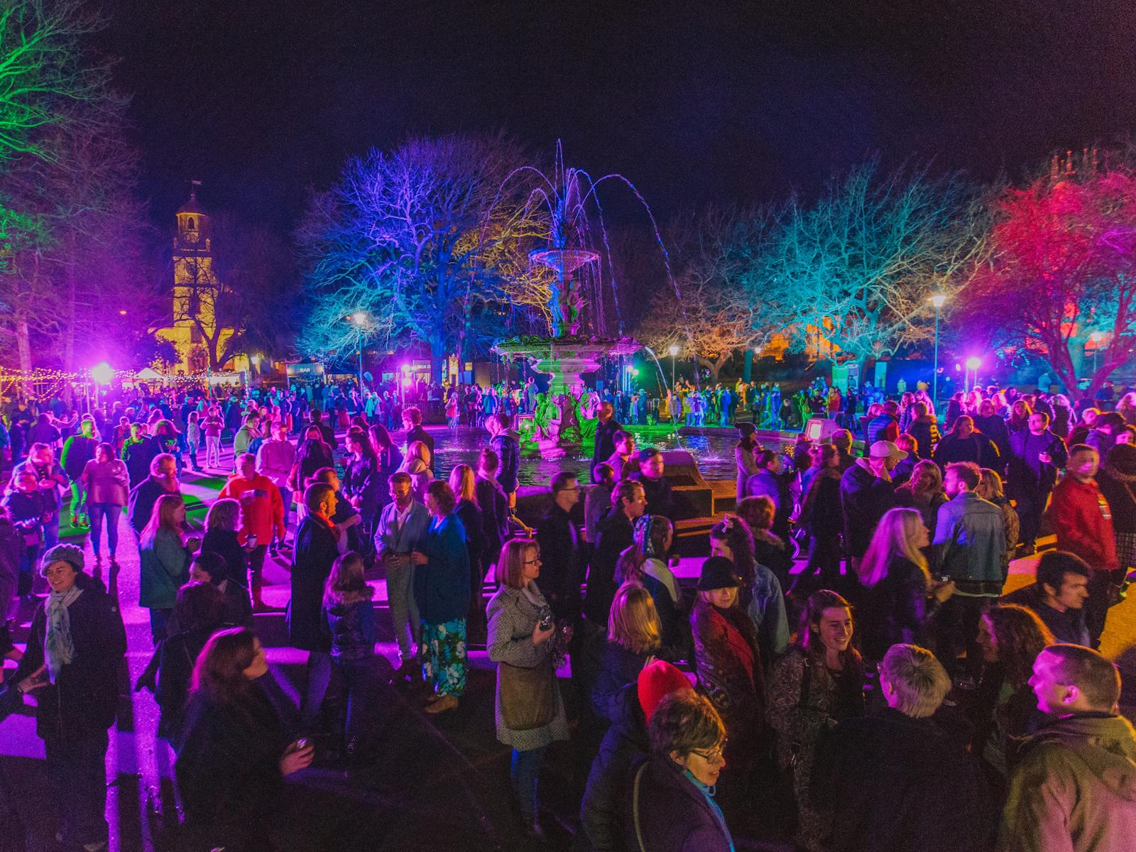 A crowd of people lit up by multicoloured lights outside at night