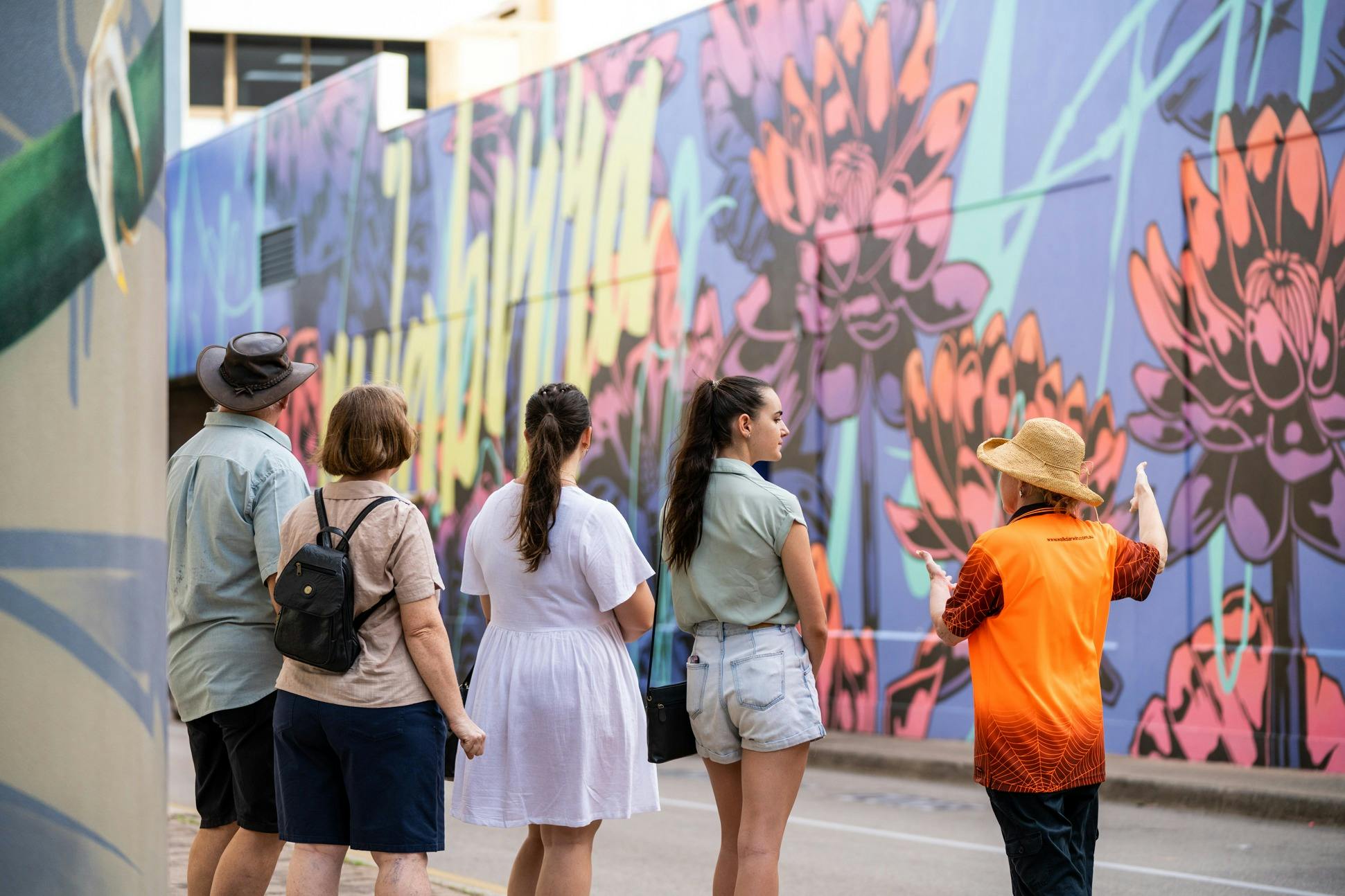 Walk Darwin guide with guests stand before a large multicolour street art mural