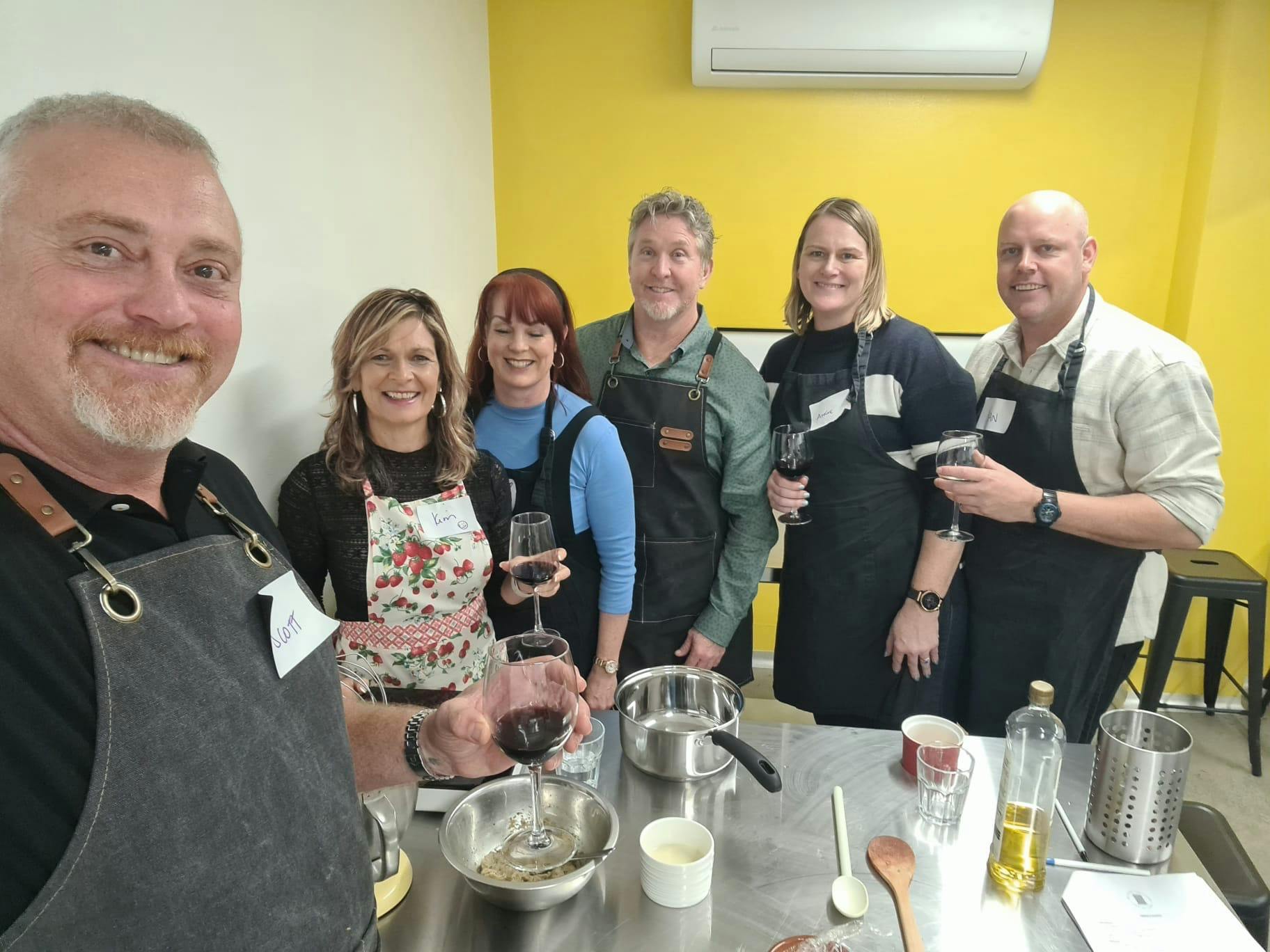 Group of people in a kitchen cooking and drinking wine