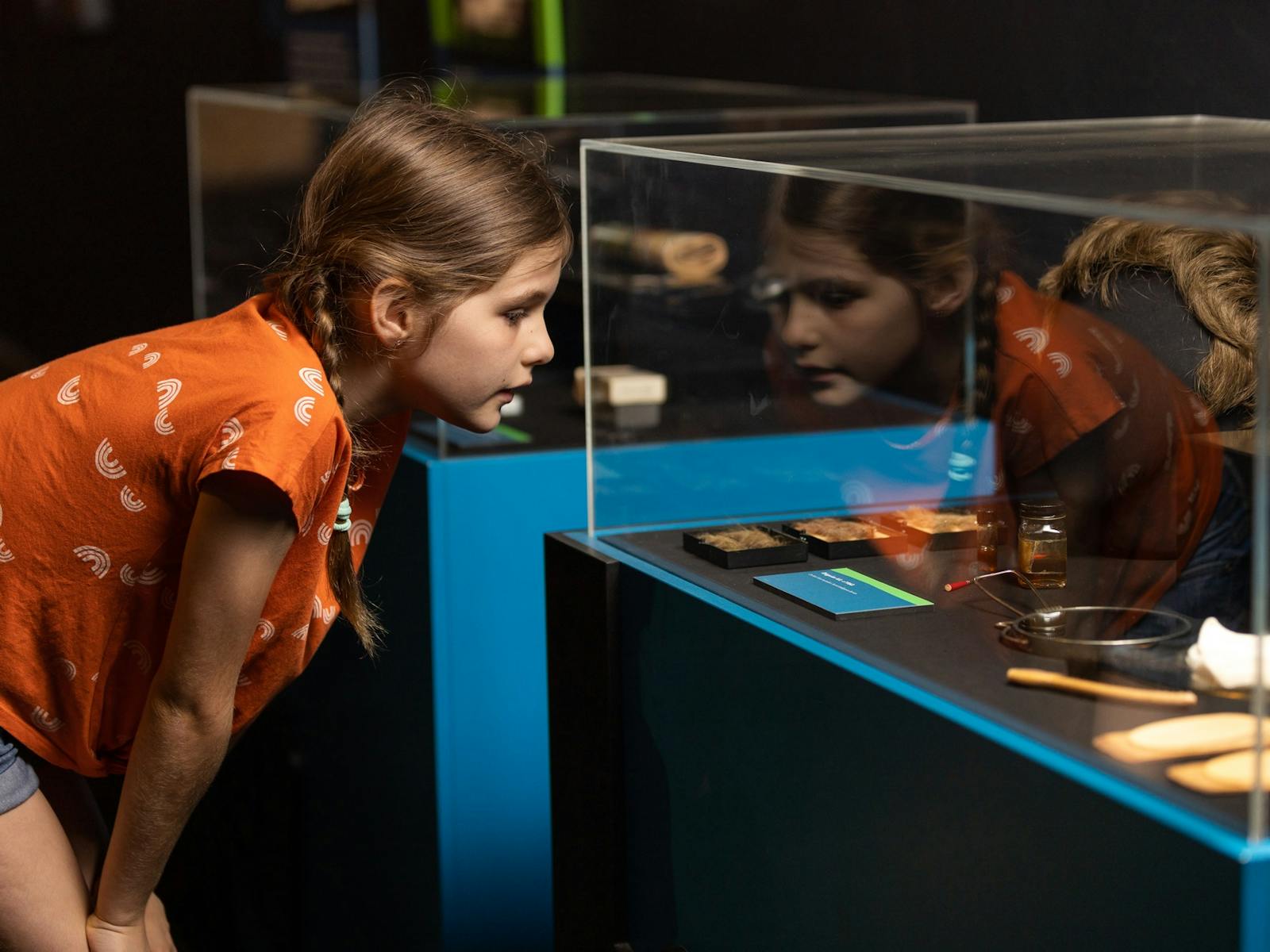 Young girl looks in exhibition clear case full of disguises and spy gadgets
