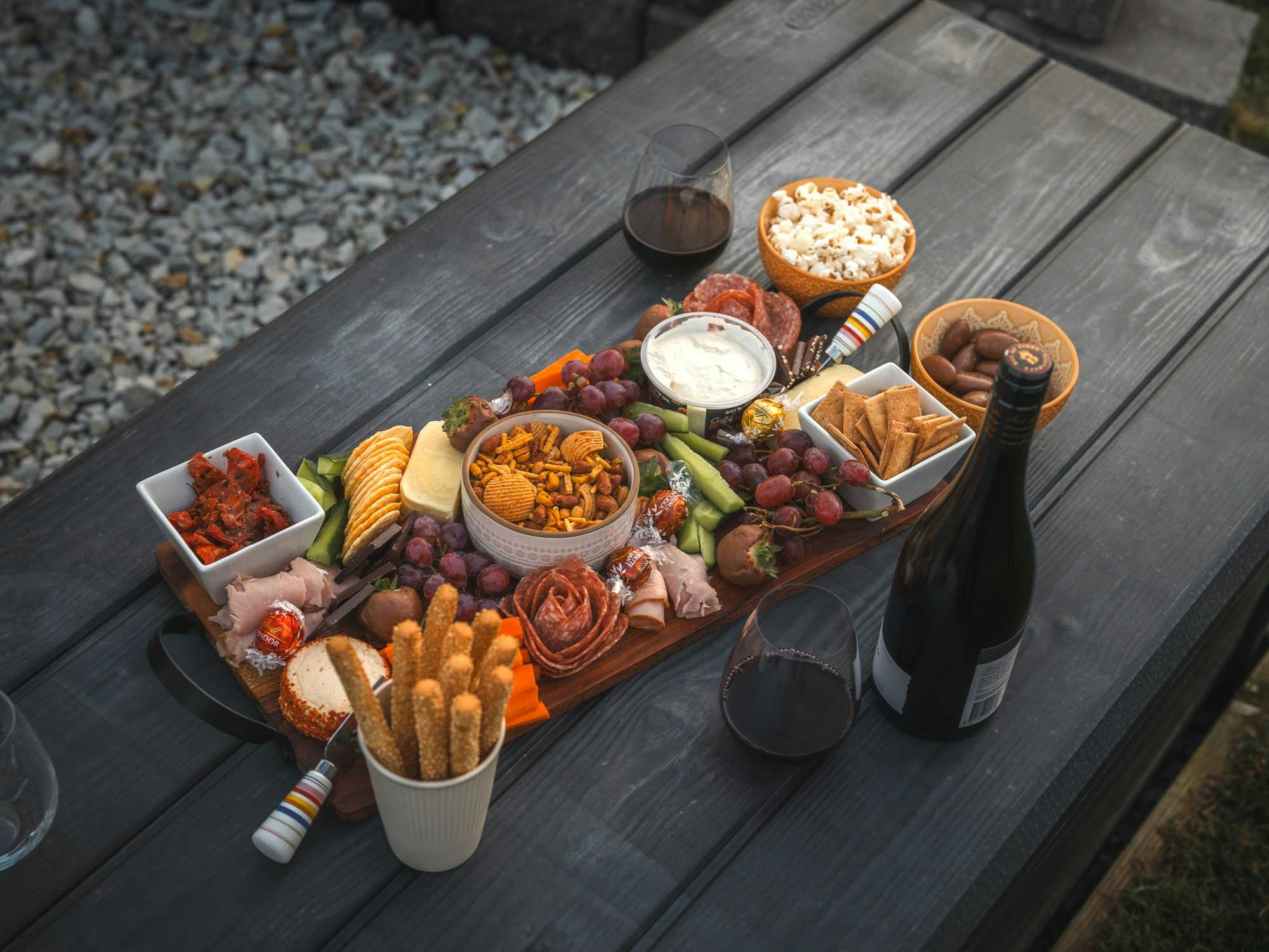 A grazing platter with local cheeses, meats, and dips served outdoors on a wooden table.