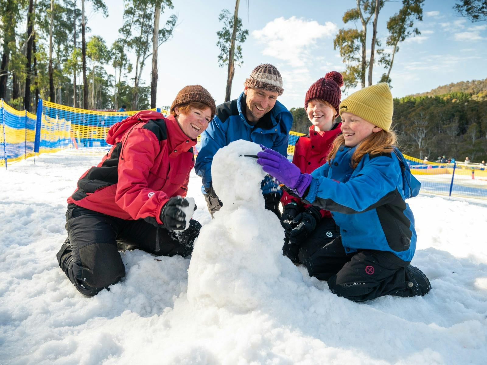 Mum, Dad, Daghter, and Son kneeling around a snowman which they are putting sunglasses on.