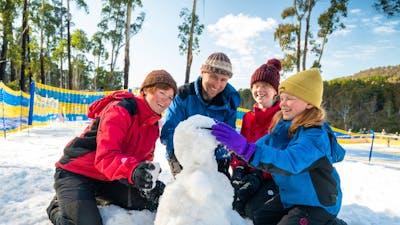 Mum, Dad, Daghter, and Son kneeling around a snowman which they are putting sunglasses on.