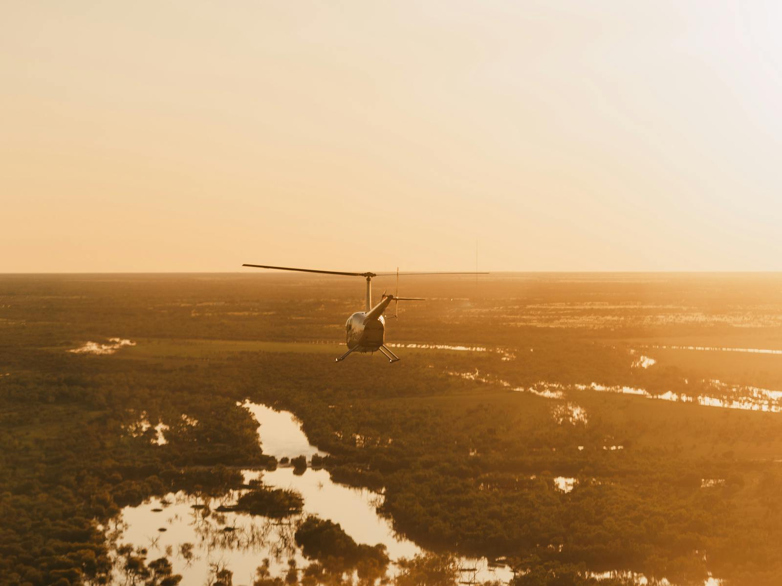 Our R44 helicopter soaring above Thomson river channel country at sunset