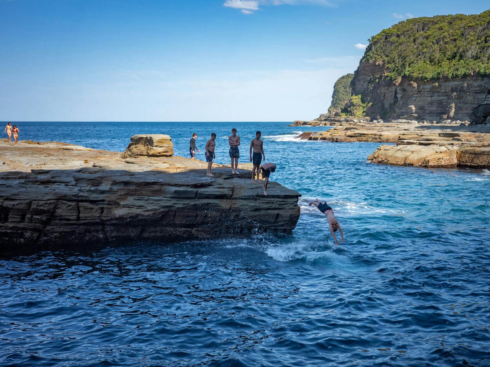 崖から海に飛び込む水泳選手たち