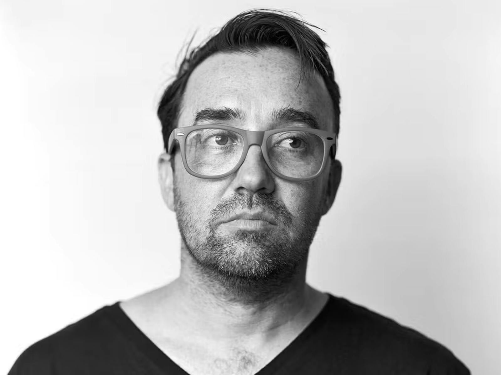 A sepia portrait of a man with glasses, looking slightly to the side. He has short hair.