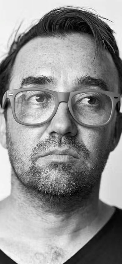 A sepia portrait of a man with glasses, looking slightly to the side. He has short hair.