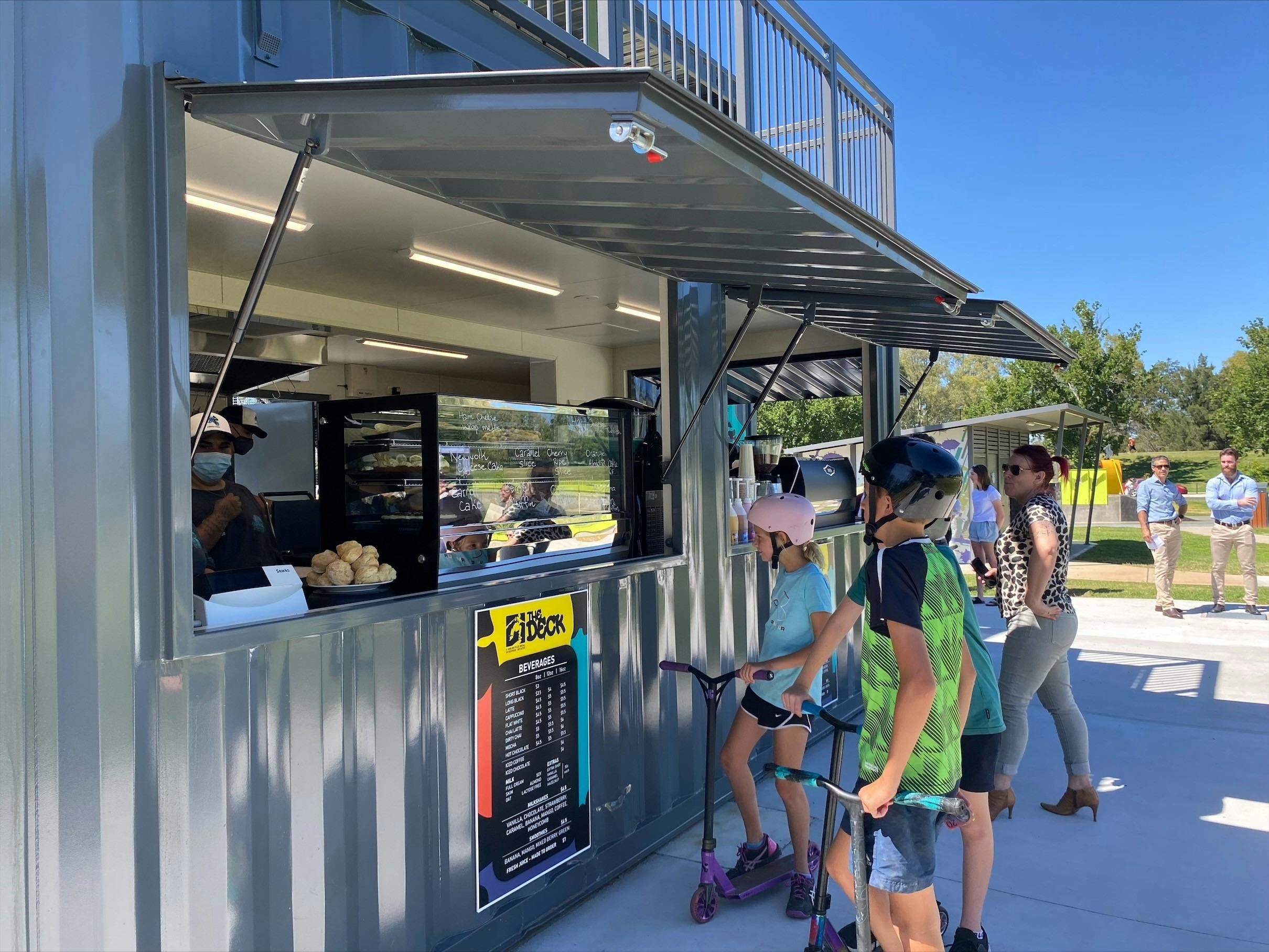 Young children with scooters and bikes order at the cafe window