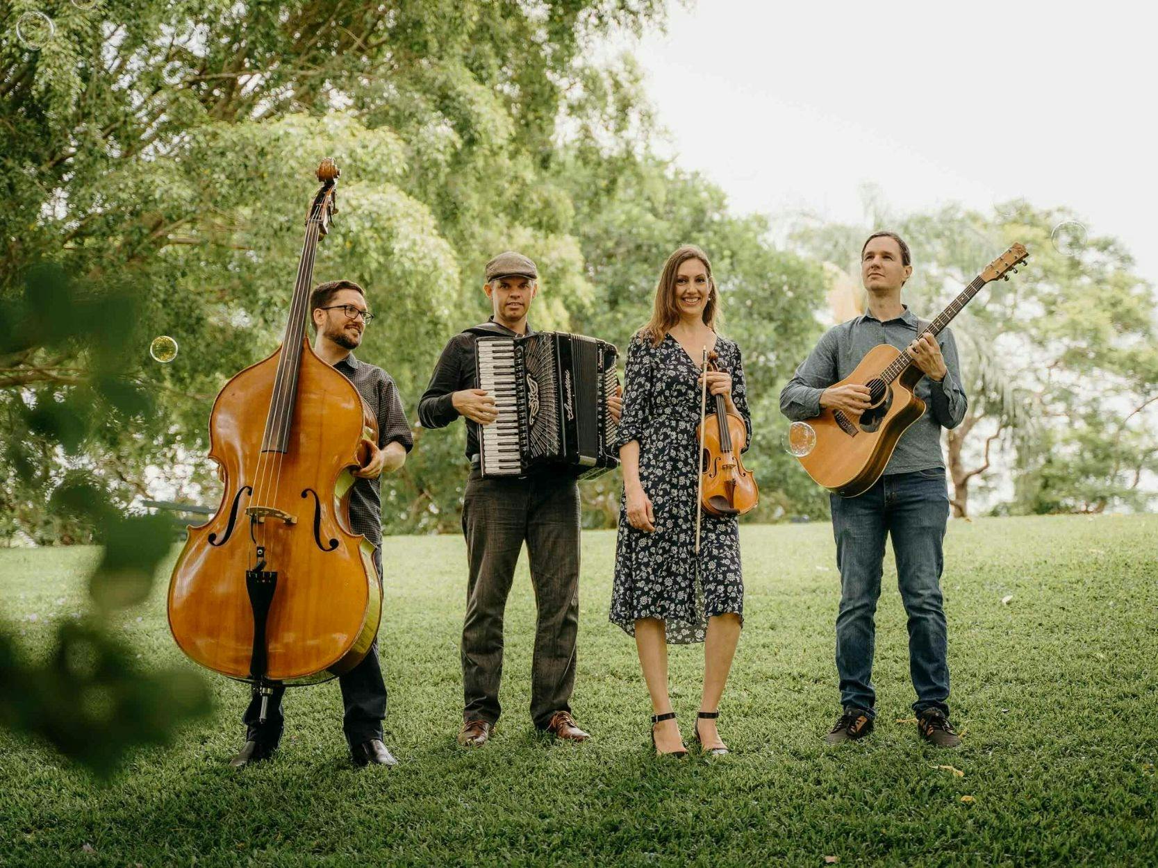 Four musicians standing on grass in a park