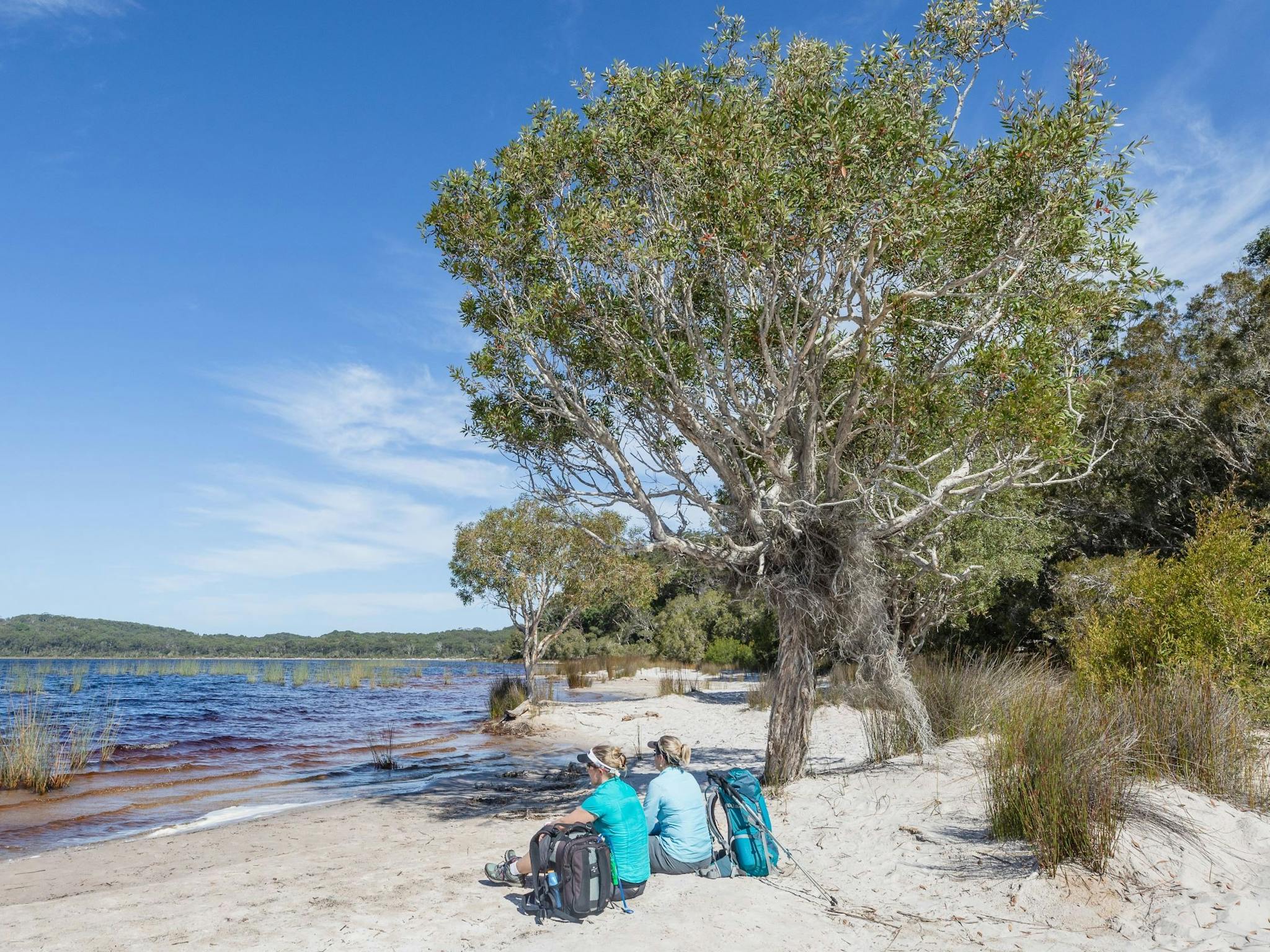 photo showing two hikers sitting on a sandy beach at Lake Birrabeen photo showing two hikers sitting on a sandy beach at Lake Birrabeen