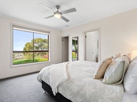 Bright bedroom with queen bed, soft tones, ceiling fan, lamps, large window with coastal views.