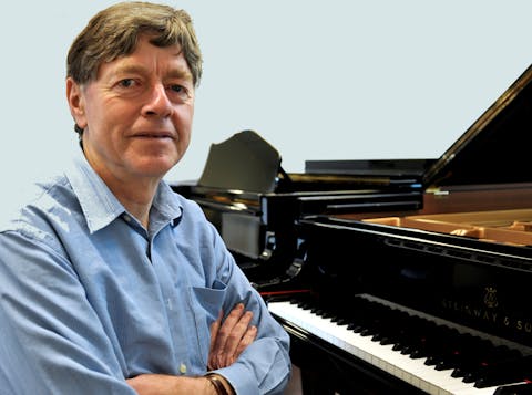 Daniel Herscovitch sitting at piano with arms folded