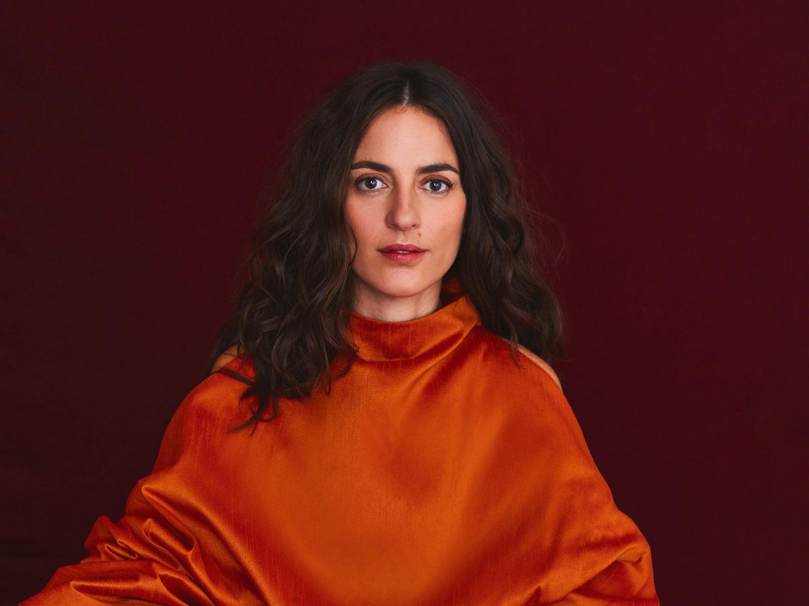 A person with long, wavy dark hair is wearing a bright orange garment.
