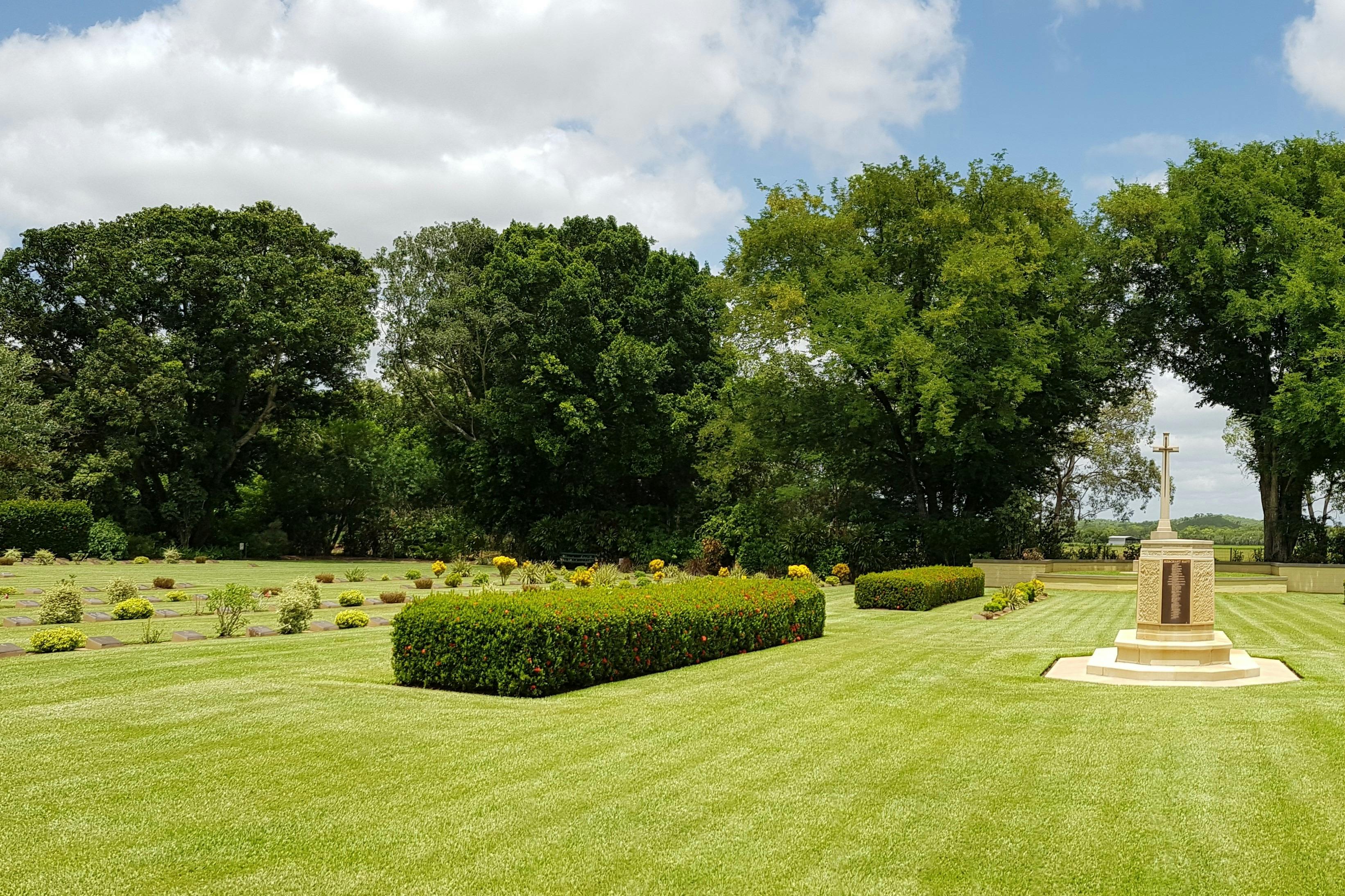 A memorial and cross sit on green lawn and boxed hedges