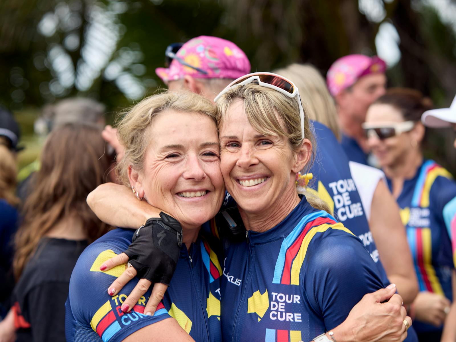 Two female cyclists embrace off-bike at the end of Signature Tour '25.