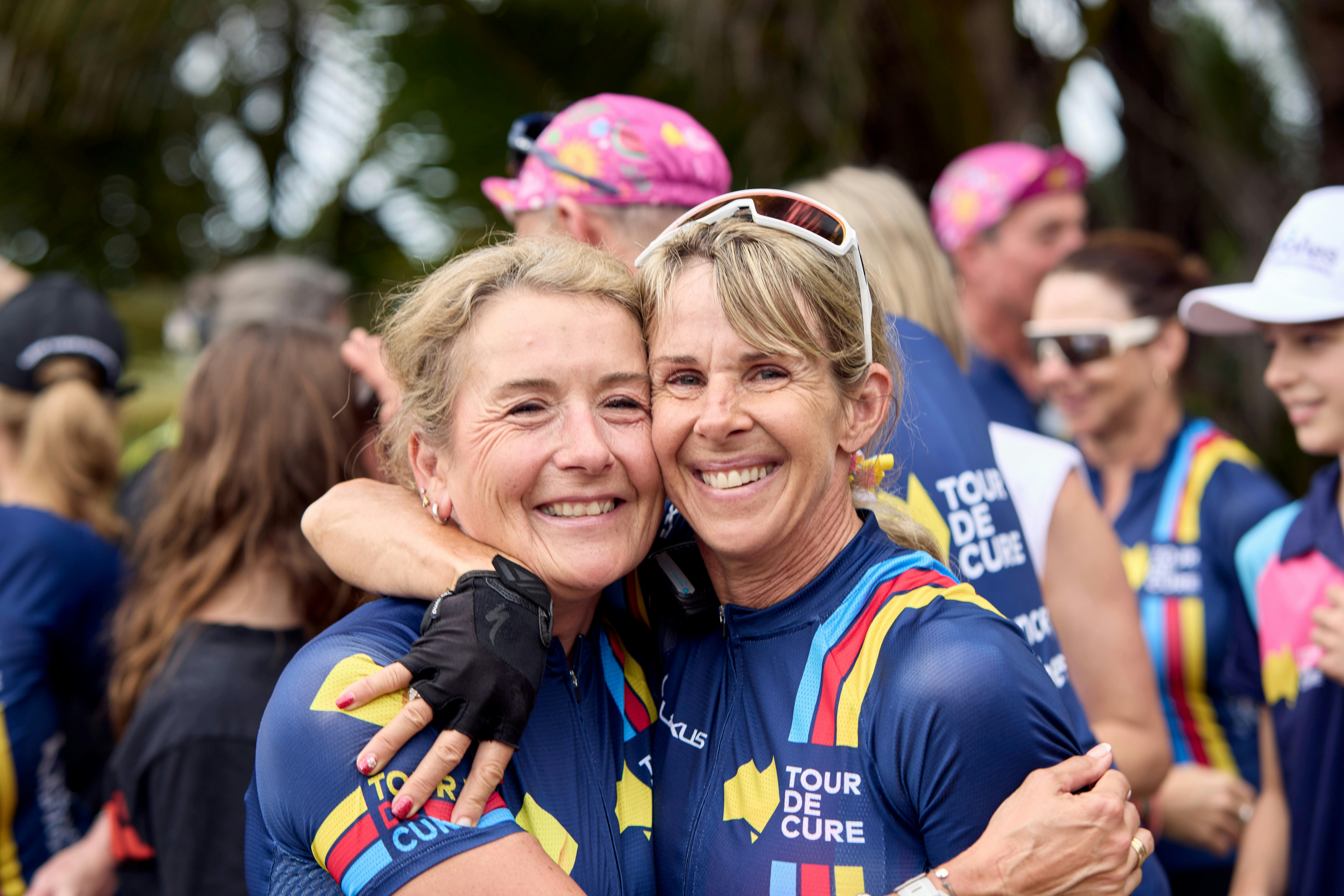 Two female cyclists embrace off-bike at the end of Signature Tour '25.