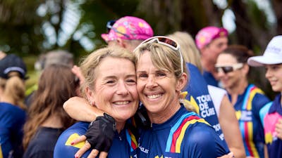 Two female cyclists embrace off-bike at the end of Signature Tour '25.