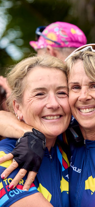 Two female cyclists embrace off-bike at the end of Signature Tour '25.