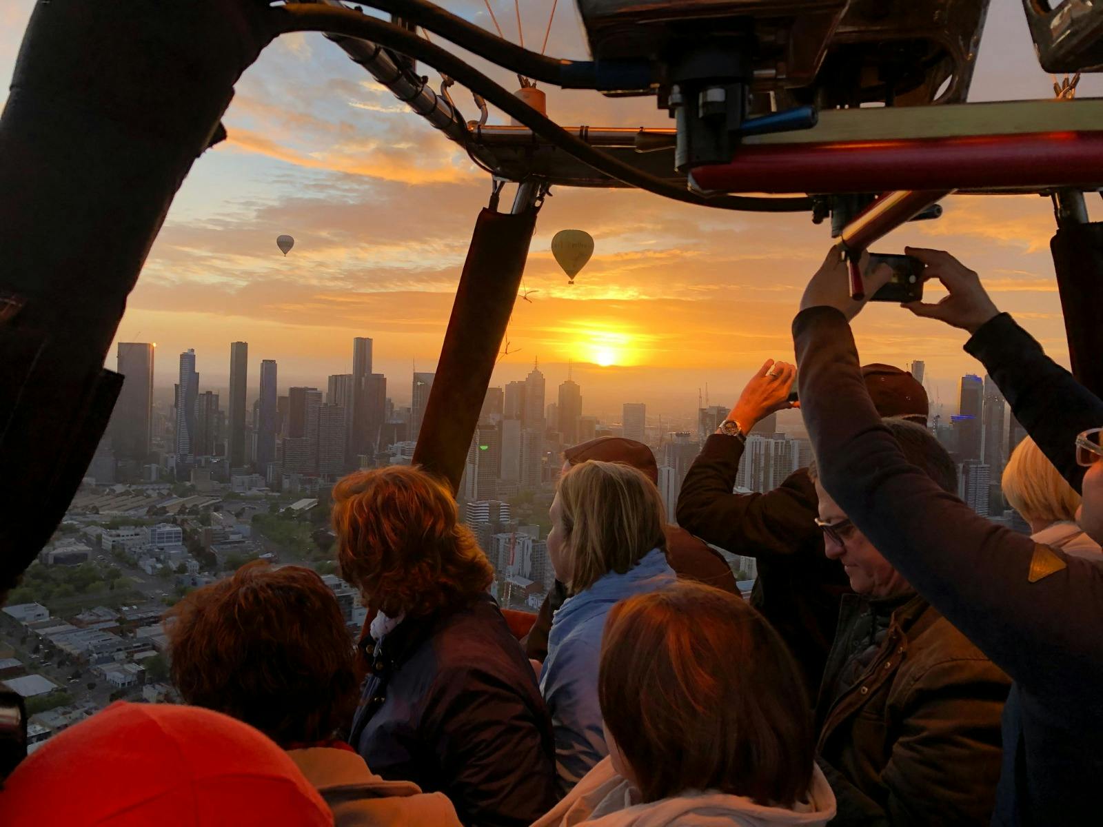 Passengers in a hot air balloon capturing photos of the city skyline and other balloons