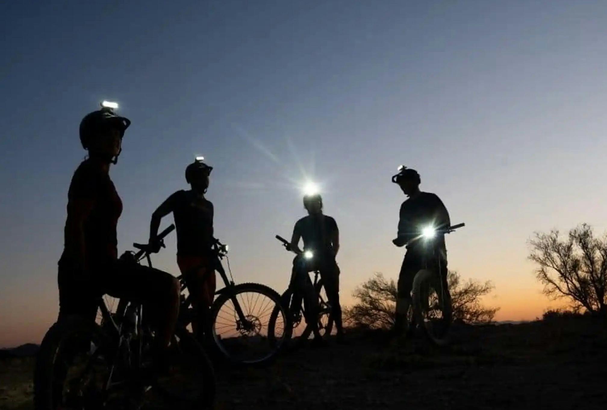 A group of riders with lights on their helmets are silhouettes against a dark background.