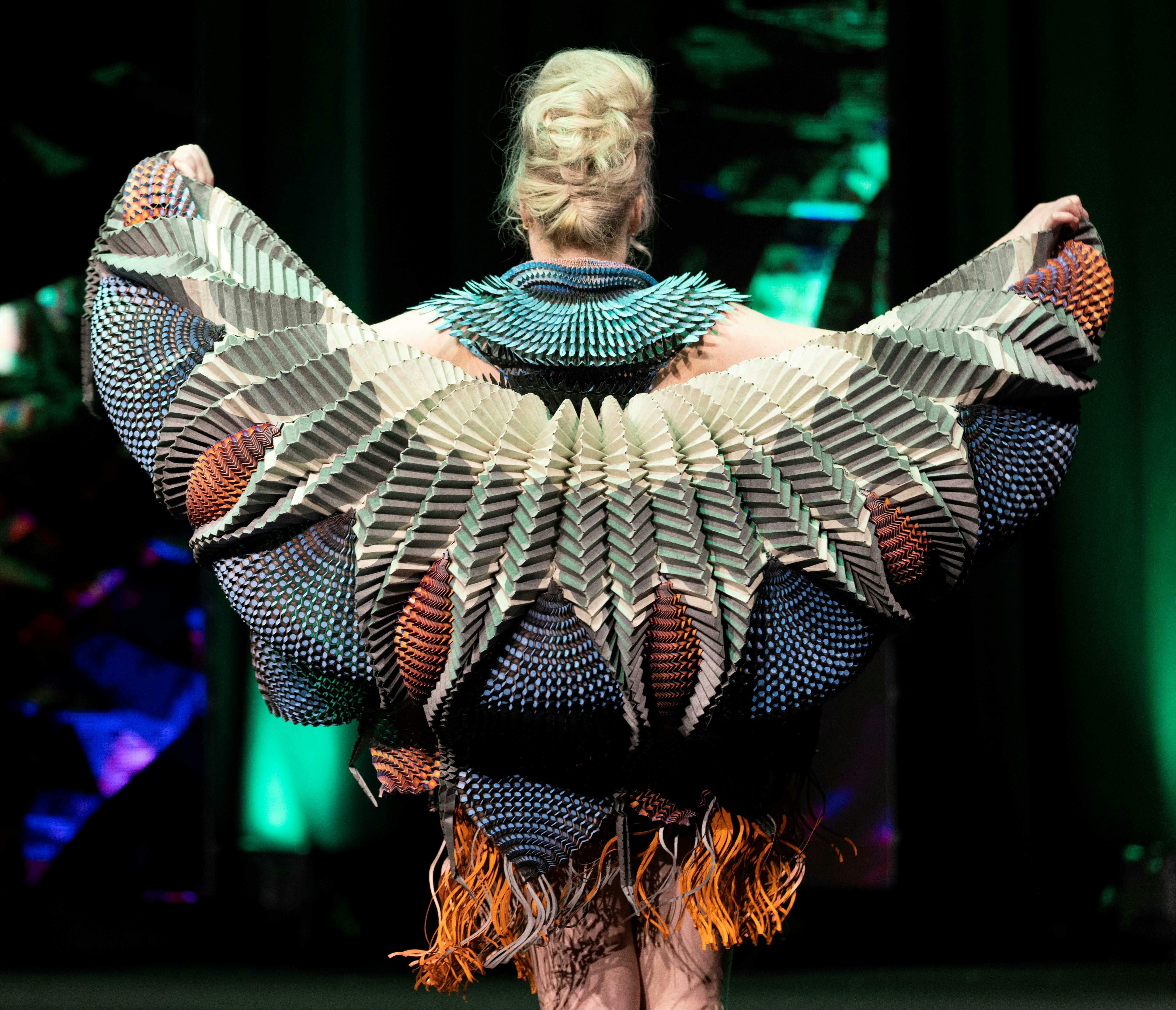 Bright and ingenious paper costume seen from behind with wing like structures fanning out.