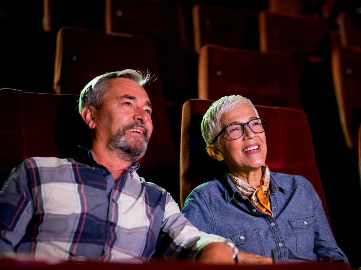 A man sitting on left and woman on right, both sitting at the cinema looking past the camera