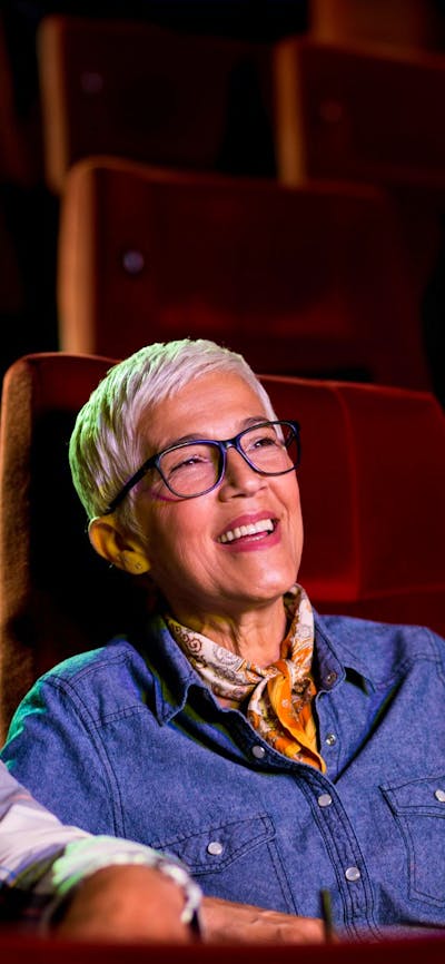 A man sitting on left and woman on right, both sitting at the cinema looking past the camera